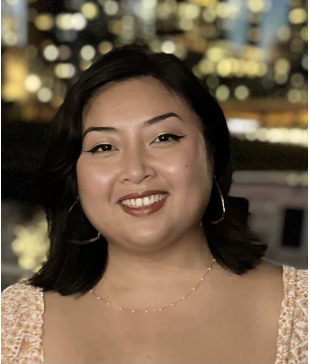 A women with black hair in an orange and white dress smiling in front of a blurred skyline. 