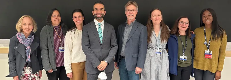 Six women and two men standing in front of a wall