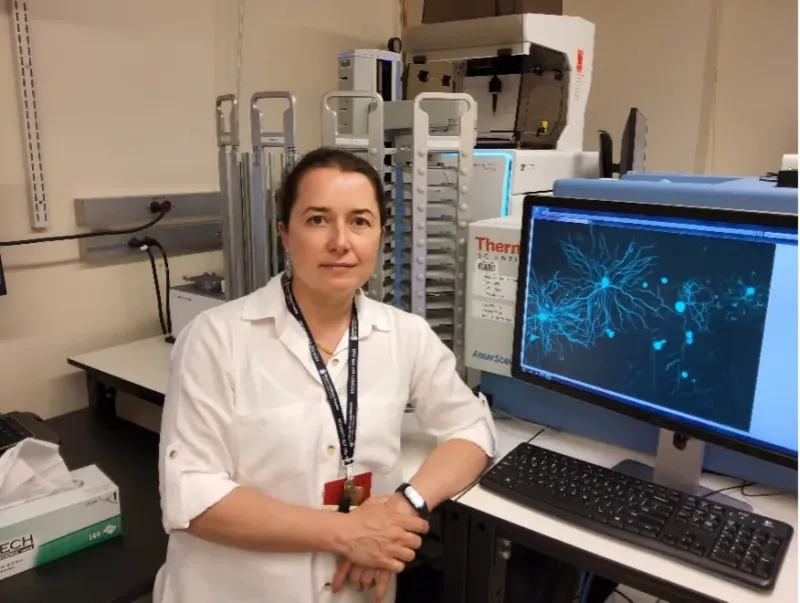 woman in a lab wearing a white lab coat sitting at a desk with a computer.