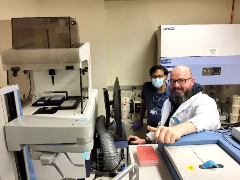 two men in a lab sitting next to a white ArrayScan™ XTI machine.