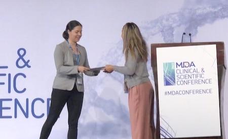 Woman on stage hands a piece of paper to another woman