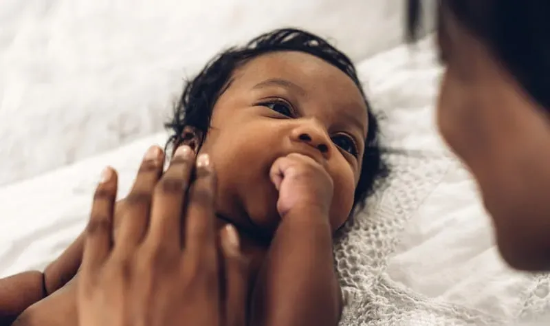 baby sucks on fist while gazing at caregiver. 