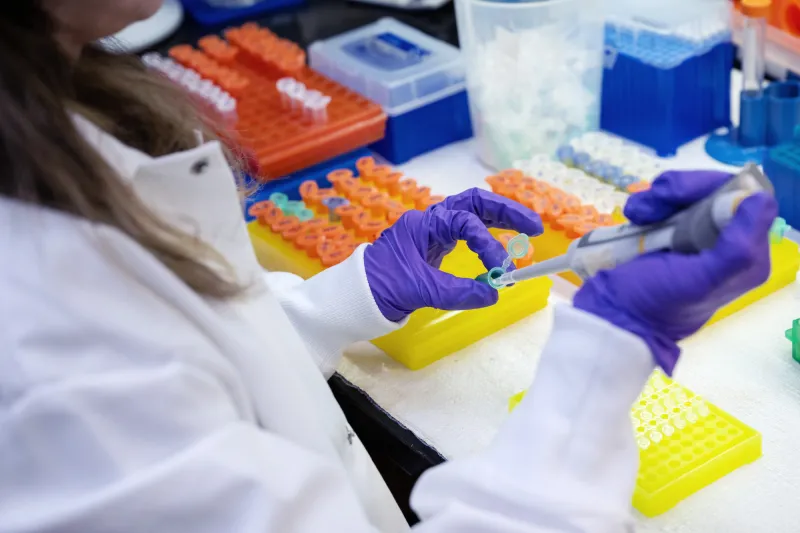 A pair of gloved hands pipe liquid into a beaker. 