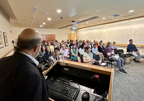 John Christodoulou speaking to a room of over fifty people sitting in chairs