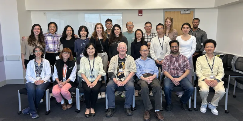 Twenty one men and women standing and sitting in three rows in a room