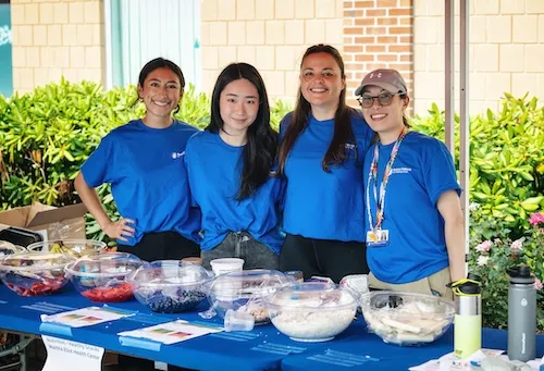Four women standing outside behind a table with bowls on top