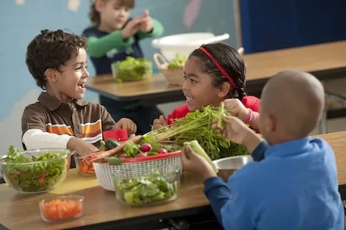 Two boys and two girls at tables with vegetables