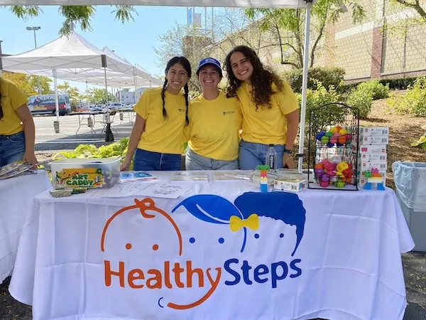 Three women standing behind a table under a tent outside