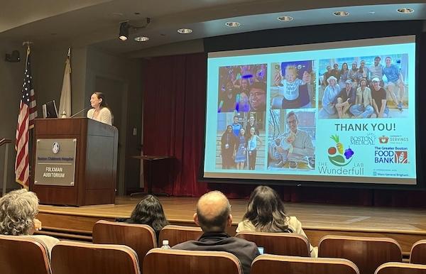 Dr. Chapman giving a presentation on a stage and four people sitting in seats