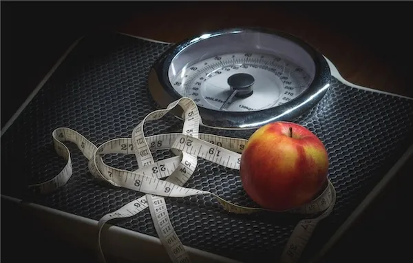 An apple and measuring tape on a scale