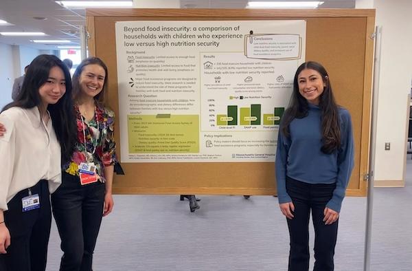 Three women standing next to a poster presentation