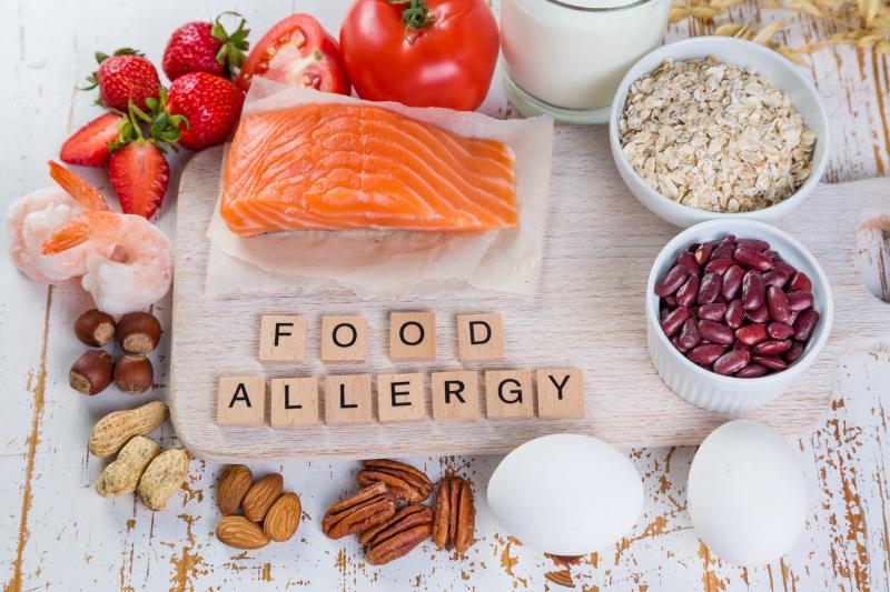 A decorative plate of salmon surrounded by fruits and grains with scrabble tiles spelling out food allergy.