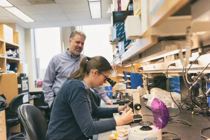Michael rogers and danielle peterse looking at something under a microscope.