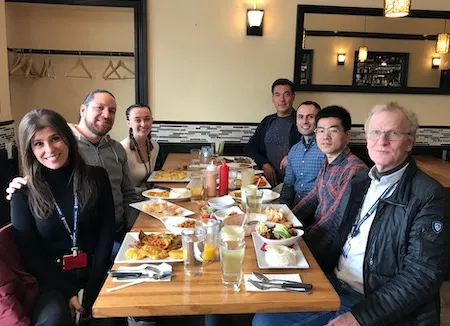 seven men and women sitting at a restaurant table with food