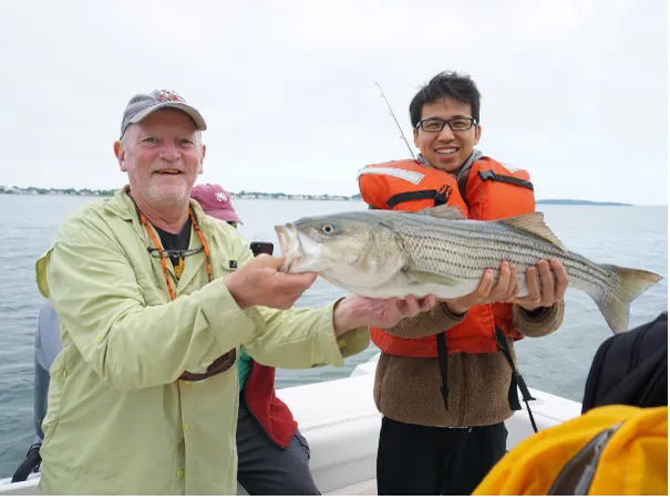 Frederick Alt and postdoctoral fellow Xiang Li on a boat holding a fish.
