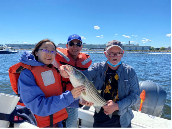 PhD student Yiwen Zhang, instructor  Hongli Hu, and Frederick Alt holding a fish on a boat.