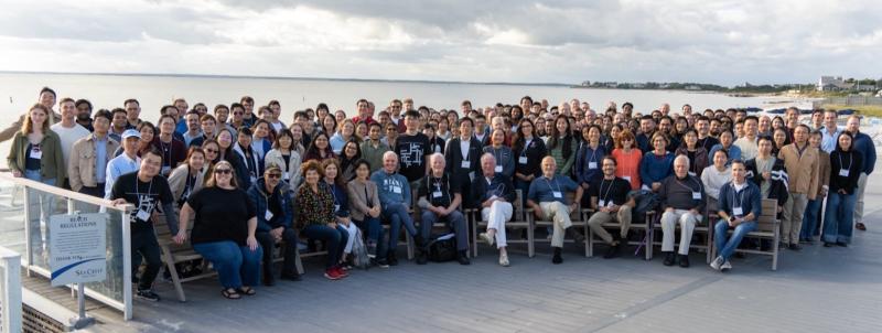 Over fifty people sitting and standing outside by the ocean