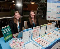 Two women sit behind a table covered with flyers. 