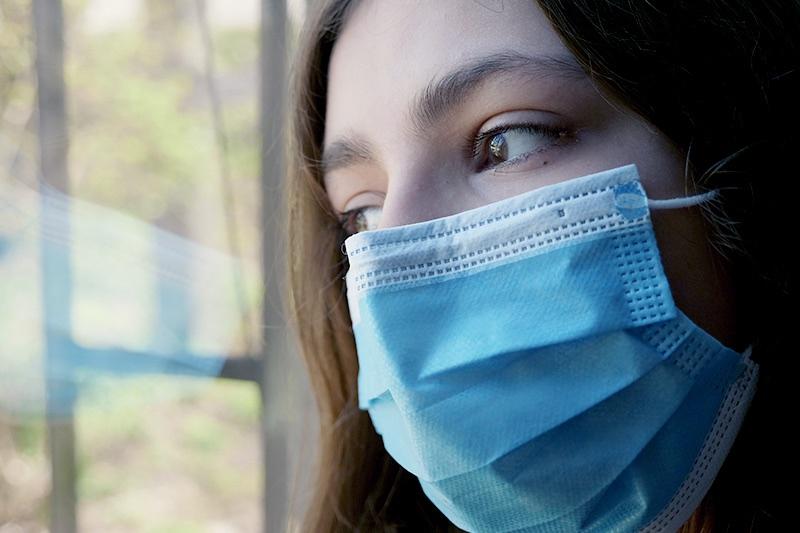 Woman wearing face mask looking out window