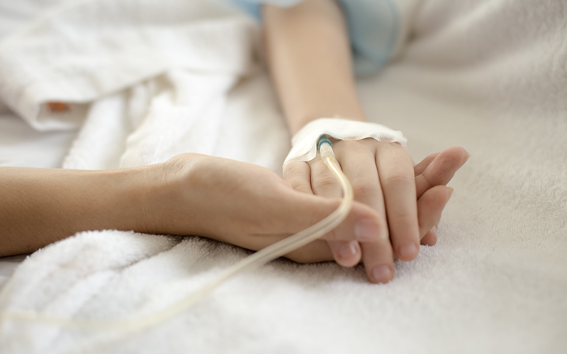 A close up of hands clasped together with a fluid tube. 