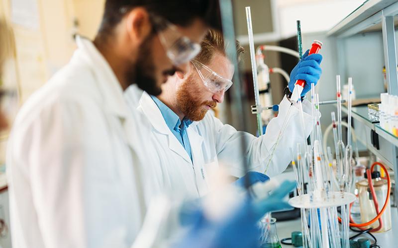 Two men stand working at a lab table.