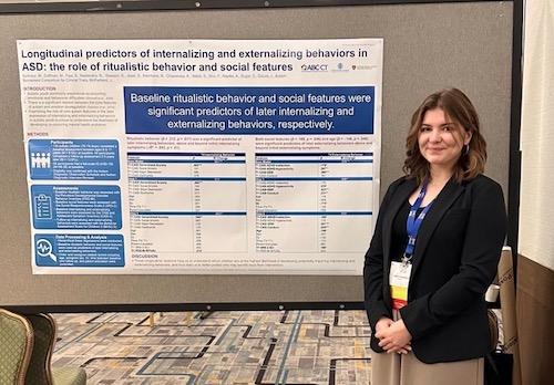 Woman with brown hair in business formal attire standing in front of a poster presentation