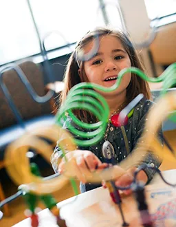 young girl in zip-up sweatshirt peeks through tabletop toy