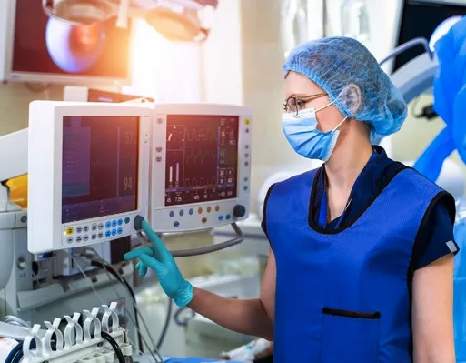 A doctor wears a blue mask and a blue x-ray weight vest while standing in front of an x-ray machine ready to press the button.
