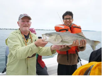 Frederick Alt and postdoctoral fellow Xiang Li on a boat holding a fish.
