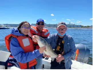 PhD student Yiwen Zhang, instructor  Hongli Hu, and Frederick Alt holding a fish on a boat.
