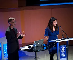A man and a woman speak up at a podium. 