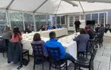 group of men and women sitting around a three tables with white table cloths in a white tent