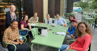 over ten women and men sitting around a green table outside having lunch