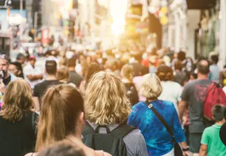 A large crowd of people in a city; the camera is behind them so you only see the back of all their heads.
