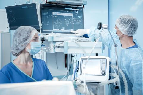 Clinician looks at monitor in operating room as another clinician looks on