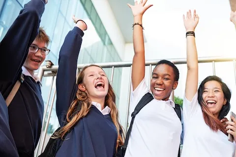 Two teenage boy and two teenage girls standing in a circle with an arm in the air