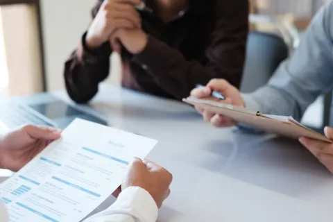 A doctor holding a piece of paper sitting across a table from two people