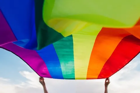 Rainbow tarp held up in the sky by two hands